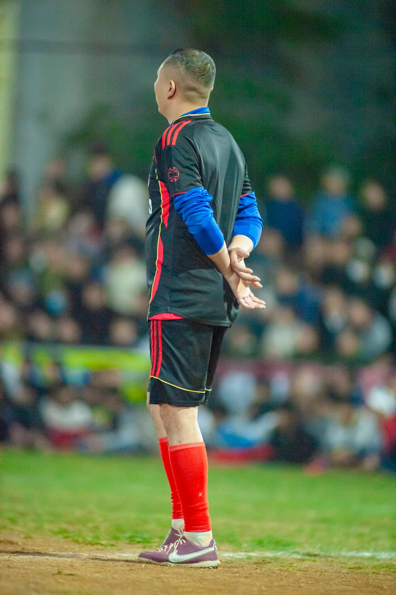Soccer coach in vibrant gear observing a match outdoors during the day.